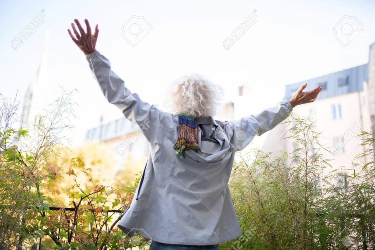 147781609 portrait from behind old woman with arms spread open outside